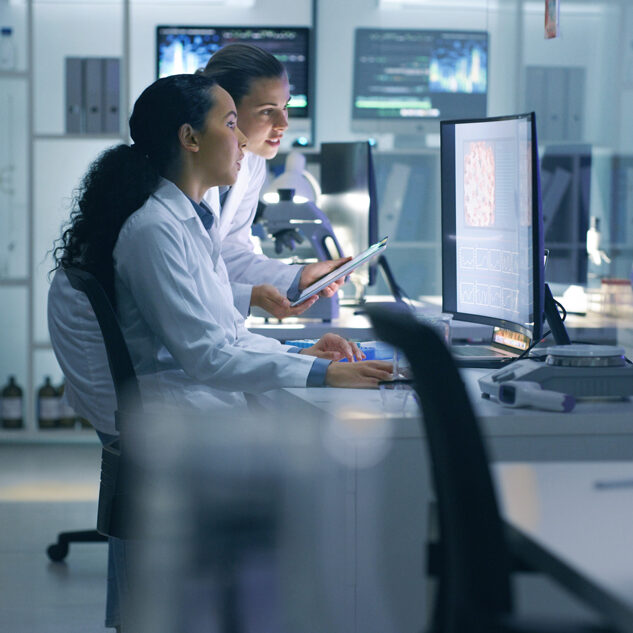 two women wearing lab coats looking at a computer