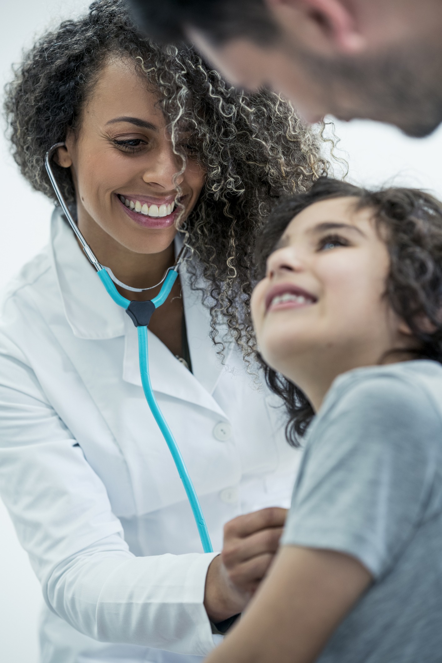 young doctor holding her little patient while they all smile and the child's father accompanies him