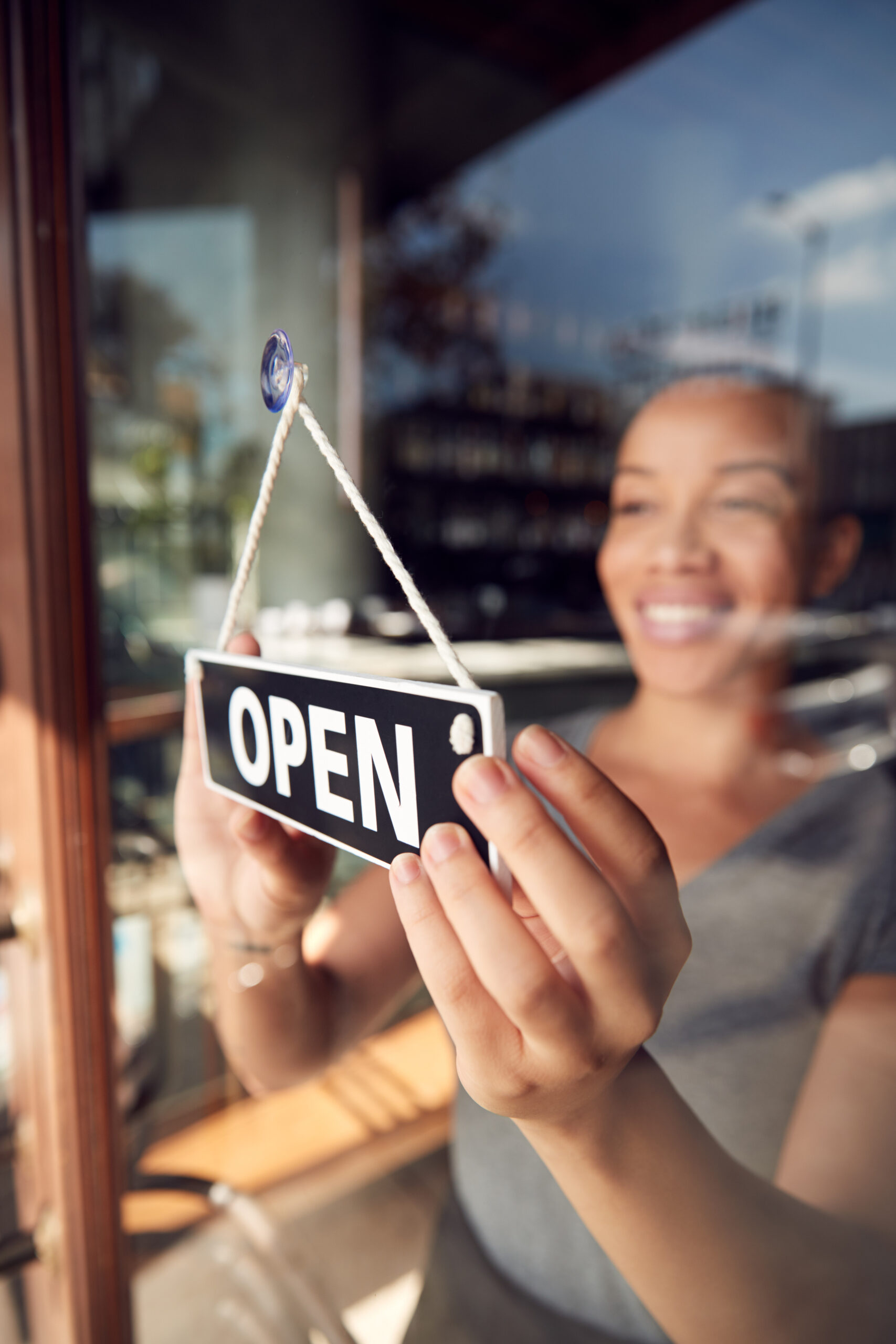 Female Owner Of Start Up Coffee Shop Or Restaurant Turning Round Open Sign On Door