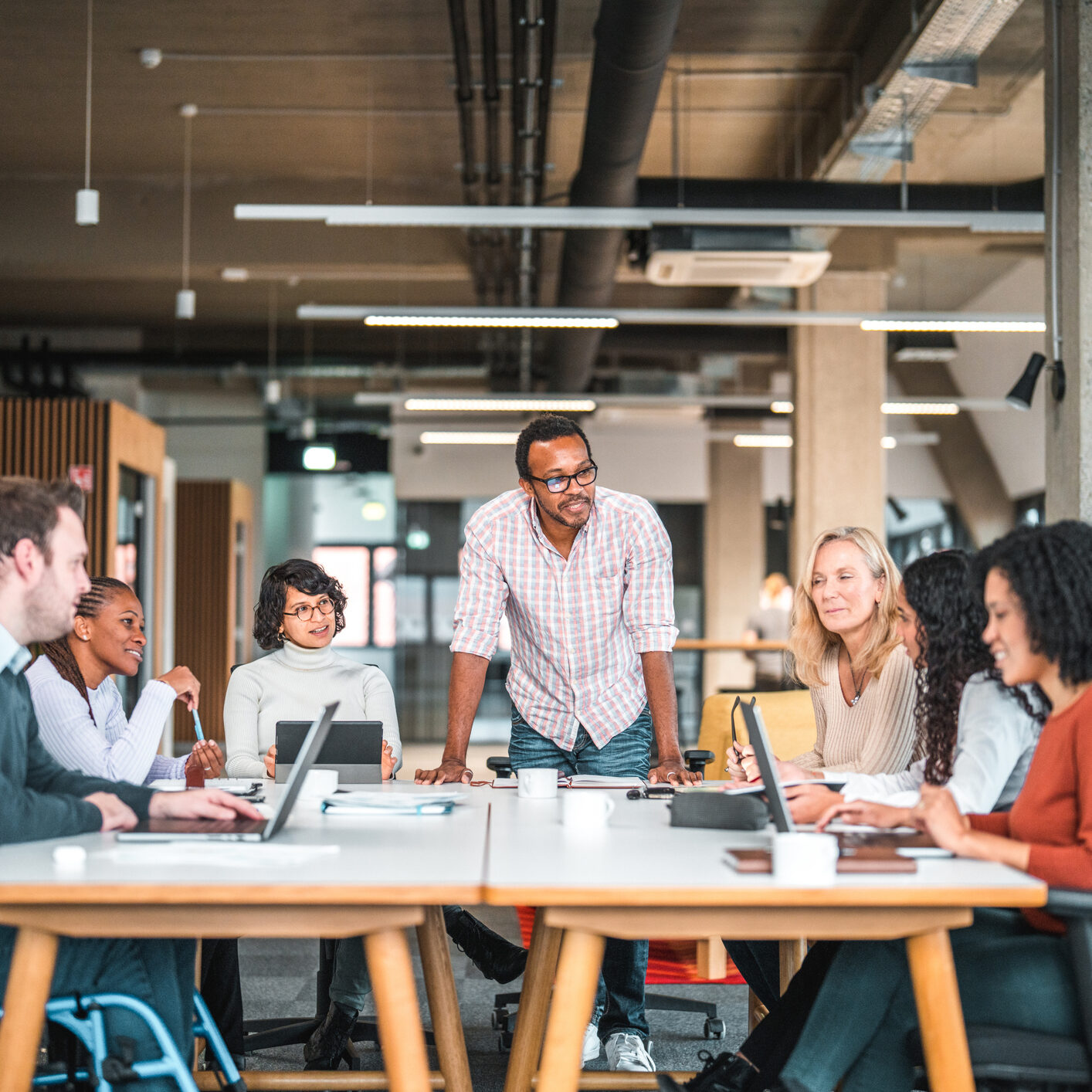 Bright, open-concept office where a meeting is being conducted with a diverse group of men and women.