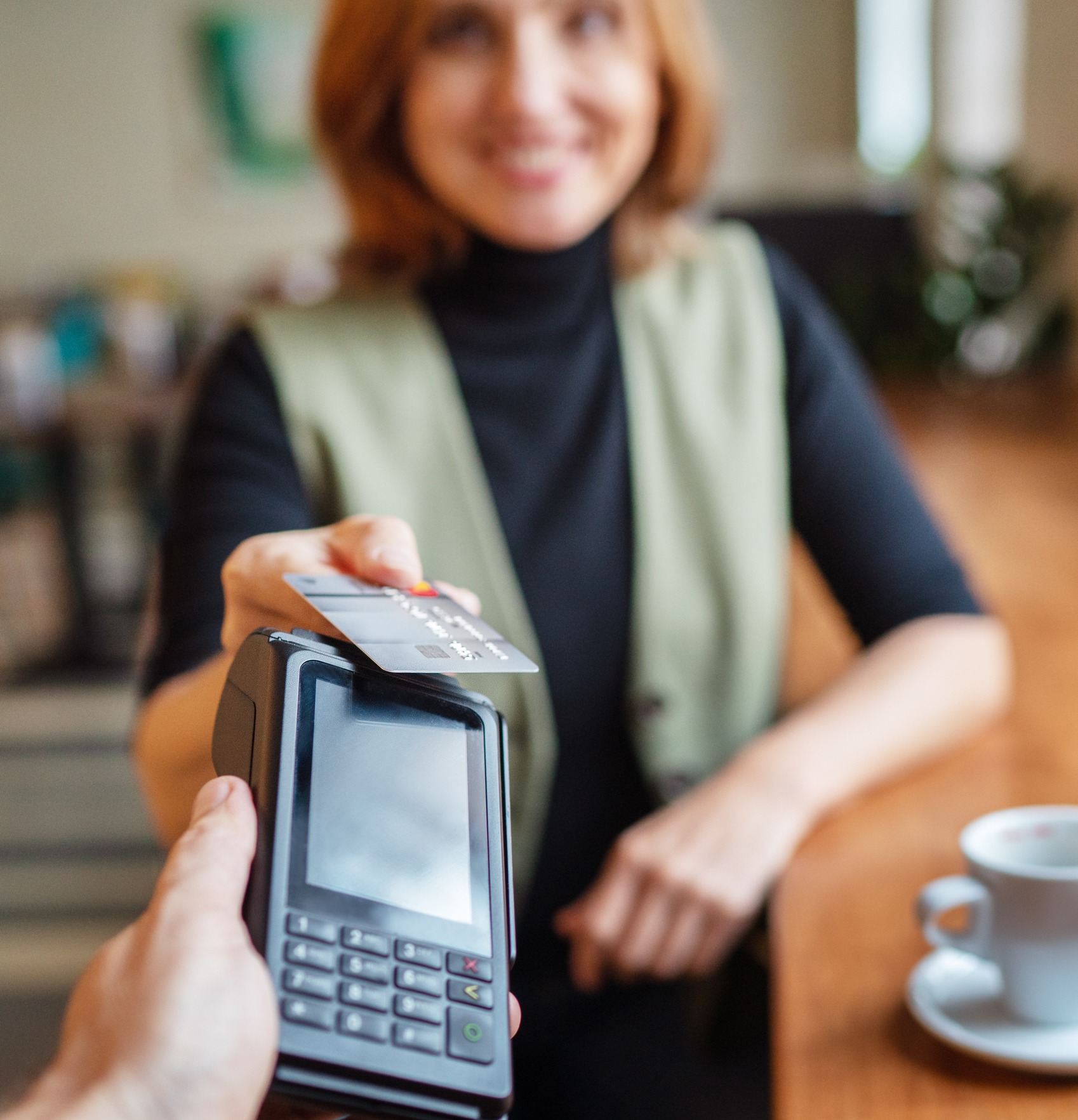 Young smiling woman doing credit card wireless bank payment with POS terminal at table in coffee shop cafe restaurant indoor. Focus on machine. Finance, restaurant industry, small business